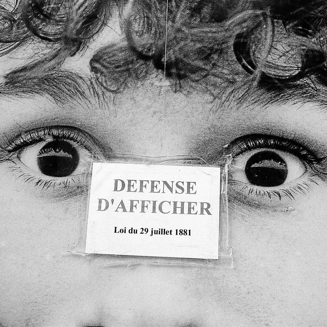 Child's eyes behind a 'Défense d'afficher' sign
